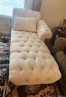 Wide view of cream chaise lounge showing tufted upholstery, pillow, and wooden legs