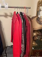 Five women's jackets hanging on a metal clothing rack showing various styles and colors including reds, snake print, black with fringe, and brown suede.