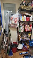 Shelving unit with various boxes and household items, ironing board and cleaning supplies visible