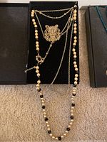Necklace featuring tiger head pendant with layered chains and pearl/black beaded necklace in box