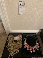 Two necklaces displayed side by side on black surface: gold-tone multi-chain Heidi Daus necklace and a floral pink and yellow stones necklace.