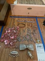 Photo of various jewelry and hair accessories on wooden surface including pink bead necklaces, silver and pink earrings, rhinestone hair clips, and bracelets.