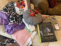 View of assorted decorative pillows, linens, books and plush throw arranged on sofa and chair.