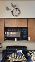 Wall clock with black and white checkered pattern and two checkerboard butterflies on the wall above microwave and stove.