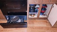 Pots and pans stored in stove drawer and cabinet, including several stacked pots with lids and non-stick pans.