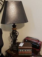 Black shade and ornate metal base lamp next to stacked book storage on a wooden table