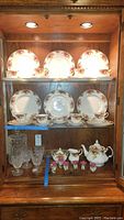 Full set of Royal Albert Old Country Roses china displayed in wooden cabinet showing plates, teacups, teapot, sugar and cream dishes, salt and pepper shakers, and napkin holders.