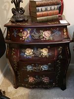 Front view showing all three drawers with floral hand painted designs and metal handles, bottom drawer missing hardware.