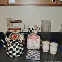 Photo showing the tea kettles, a metal pitcher, glass vase, salt and pepper shakers, a decorative house-shaped tea pot, and napkins arranged on countertop.