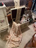 White wood lined storage trunk open on floor with lace throw draped over edge and porcelain doll inside