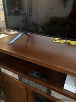 Top surface of the wooden cabinet showing a TV stand leg and a remote control placed inside one of the cabinet shelves below.