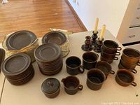 Overview of all stoneware items on table: plates in front, mugs and small pieces at right