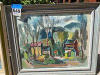 Rustic landscape painting in wooden frame showing houses and trees with autumnal colors, broad brush strokes.