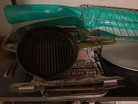 View showing cast iron grill skillet, metal roasting rack, and other bakeware items stacked behind