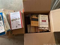 Top view of an open box showing hardback books titled 'Secret Ingredients' and 'The Best of Times America' by Haynes Johnson along with other books.