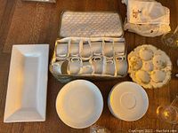 Photo showing 12 white china tea cups in fitted case, 11 saucers, 9 small plates, and white rectangular platter at left