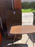 Two laminate folding tables shown standing vertically in garage, one large 24 x 48 inches and one smaller folded table in front.