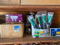 Box and open packages of outdoor lightbulbs and multiple unopened packages of 8-inch zip ties in wooden shelf