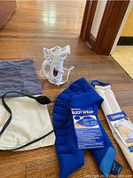 Photo showing two heating pads, a white handheld steamer device, and a gray cloth pouch all placed on a wooden floor
