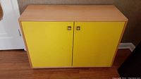 Front view of maple veneer cabinet with two yellow doors and silver square pulls