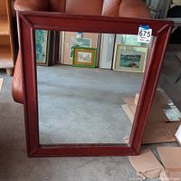 Red wood framed mirror standing, showing frame style and size relative to nearby chair and surroundings.