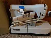 Side view of white Necchi Lyra sewing machine with power cord wrapped around it and a paper manual inside the carrying case under the machine.