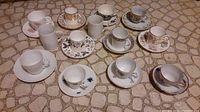 Photo showing variety of 11 cup and saucer sets and 2 loose cups arranged on patterned surface.