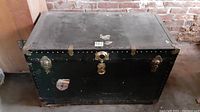 Front view of vintage black Marine Corps travel trunk showing studded metal edges, central lock without key, two side latches, and paint wear.
