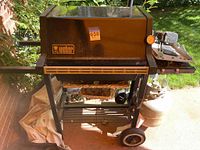 Photo showing the full Weber gas grill in black with lid closed, positioned outdoors on a patio with two wheels and side tray visible.