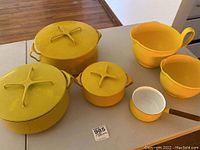 Three yellow enameled Dansk lidded pots and small saucepan, two yellow melamine bowls on table