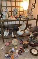 Wide view of figurines and decorative items on multi-level shelving, including animal figurines, small boxes, crowns, and a candle with blessing message. Carpeted floor showing larger pieces.