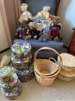 Photo showing a group of approximately twelve Boyd teddy bears seated on a chair, along with three natural woven baskets with handles, two lidded woven baskets, three nesting floral bins, and one painted tin container with pansy flowers.