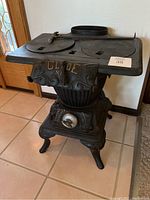 Full view of the antique cast iron stove showing the front and top surface with stove lids and flue opening.