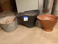 Three coal buckets/bins in a basement setting showing their overall shape, color, and condition.