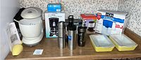 Full lot displayed on kitchen counter showing white Westinghouse stand mixer, Mr. Coffee coffee maker box, Farberware hand mixer, Pure Water pitcher in box, travel mugs, Pyrex casserole dishes, and coffee filters box.