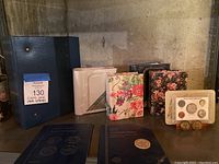 Five photo albums in varied colors including blue, beige, and floral patterns along with two Whitman coin albums and coin plaques