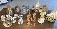 Group shot of Dickens Miniatures village buildings, ANRI wood carved figurines including a bunny and child with lamb music box, assorted small house ornaments and figurines on a wood surface.