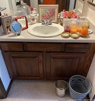 Bathroom countertop with Ethan Allen floor mirror reflection showing assortment of bathroom accessories including pink floral arrangement, candles, glass jars, vanity mirrors and decor items.