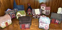 Group photo showing all 10 unique fabric house boxes arranged on a wooden surface, highlighting distinct colors and textures of handcrafted needlework and fabric designs.