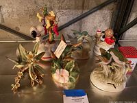 Six figurines displayed on a table against a concrete wall background, featuring hummingbird and childhood themes.