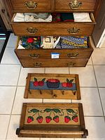 Wooden folk art towel holders displayed on the floor, two drawers above containing assorted folded linens including hand towels and tablecloths in various colors and patterns