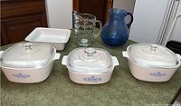 Photo of two Corning Ware casseroles with lids and two glass pitchers on countertop