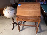 Photo showing the closed wooden secretary desk with the Replogle globe on stand beside it on concrete floor.
