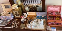 Wide view of table showing multiple jewelry boxes (floral fabric, wood, vinyl, velvet gift boxes), jewelry pieces, trays, ceramic and glass containers, trinket box and clock