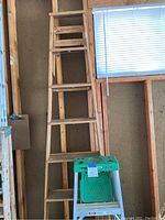 Wooden folding ladder with small green plastic step stool in front.