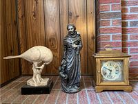 All three items displayed together on brick floor: Saint Francis sculpture, bird sculpture, Waltham clock.