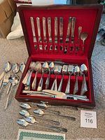 Two sets of silverware with forks, spoons, knives displayed in a red lined wooden case with some pieces arranged outside the case.
