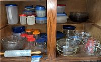 Shelves containing various glass pie baking dishes, glass mixing bowls, assorted storage containers, and a marble rolling pin