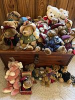Photo showing the assembled teddy bears displayed on and in front of the wooden trunk, highlighting varying sizes and clothing details.