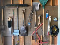 Wide shot of all hanging yard tools on pegboard including shovels, rake, broom, pitchfork, saws, extension cord, levels, hand tools